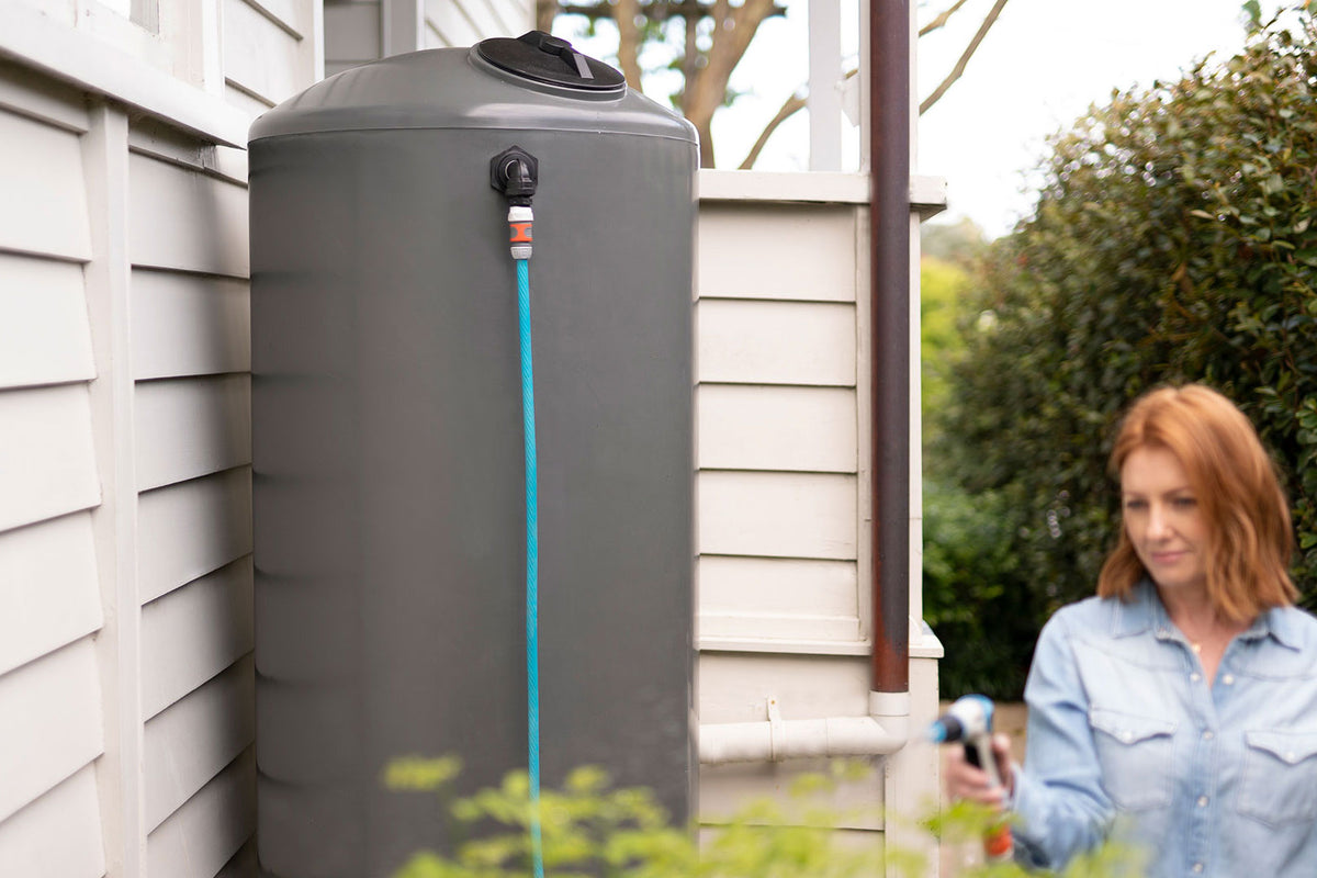 Lady uses a garden hose atatched to a Bailey icon range slim urban rain water harvesting tank outside her house